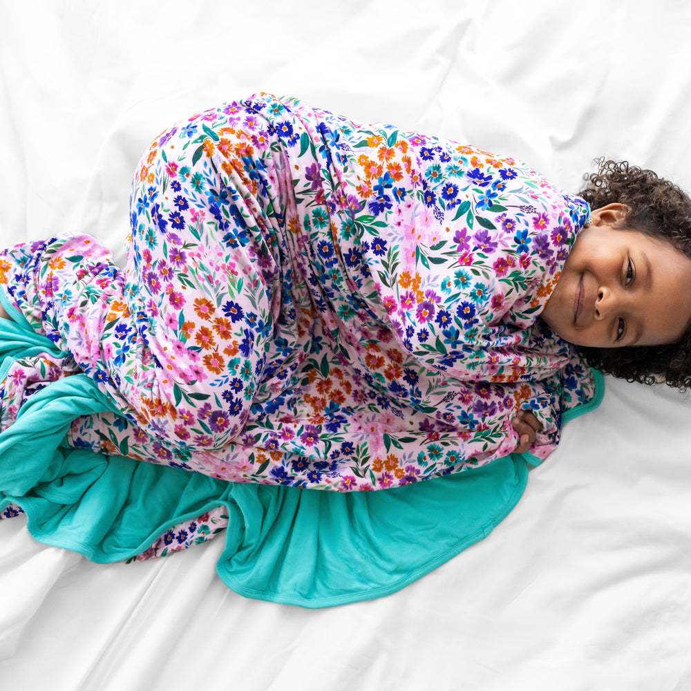 Image of a child wrapped up on a bed wearing a Sweet Pea Floral Cloud blanket