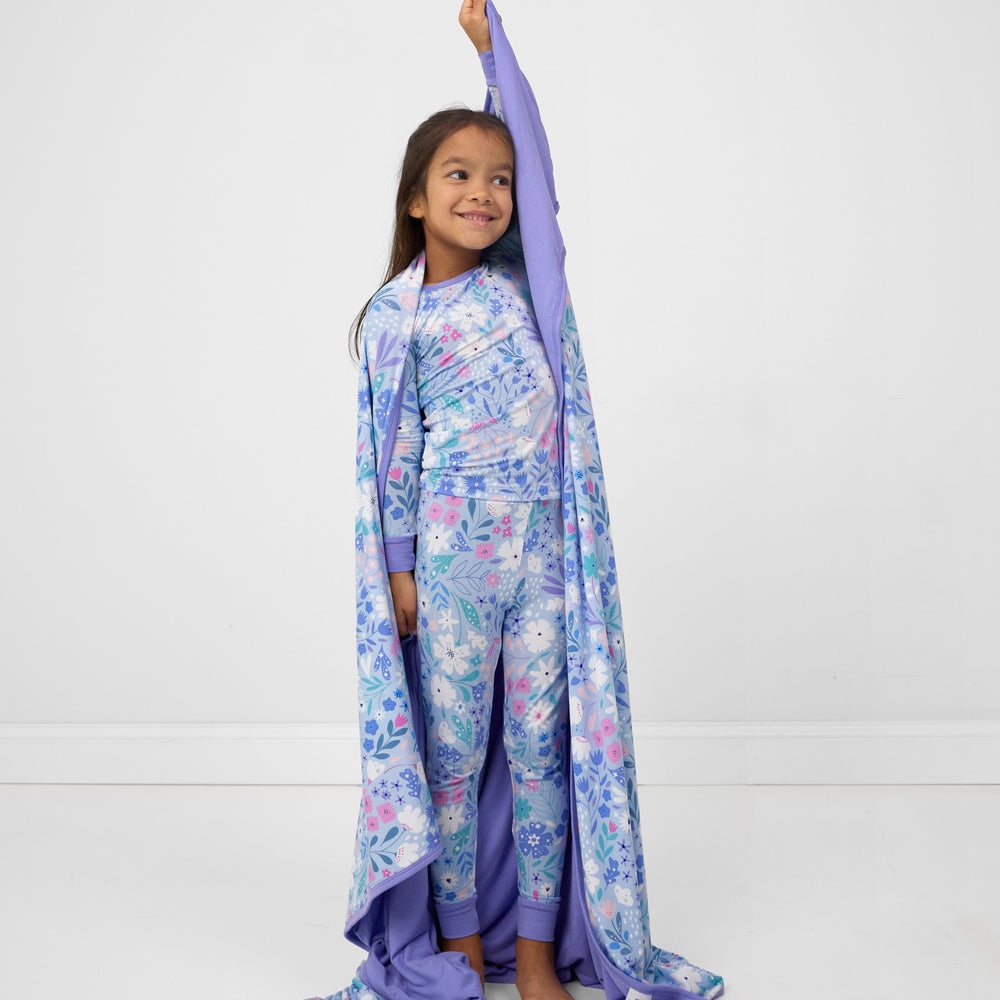 Image of a child holding up a Magical Meadow cloud blanket wearing a matching two piece pj set