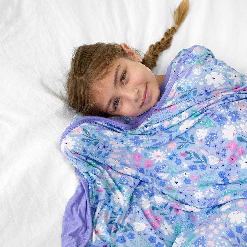 image of a child laying on a bed cuddling under a Magical Meadow cloud blanket