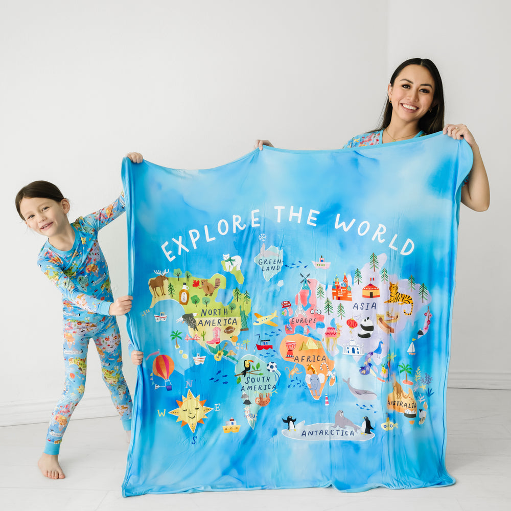 mom and child holding up an Around the World cloud blanket. Child is wearing a matching ARound the world printed two piece pajama set
