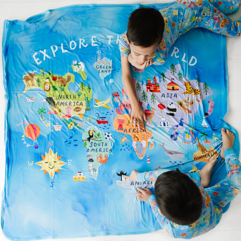 Children sitting and playing with an Around the World cloud blanket. Kids are wearing matching Around the World two piece pajama sets