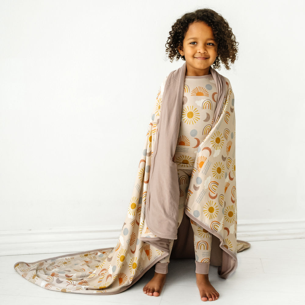 child wearing Desert Sunrise two piece pjs pants with a matching printed large cloud blanket over her shoulders