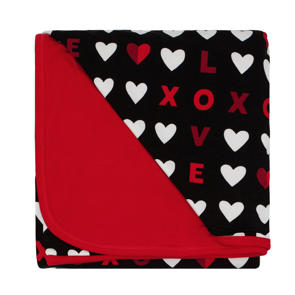 Click to see full screen - Flat lay image of a Black XOXO large cloud blanket showing the solid red backing