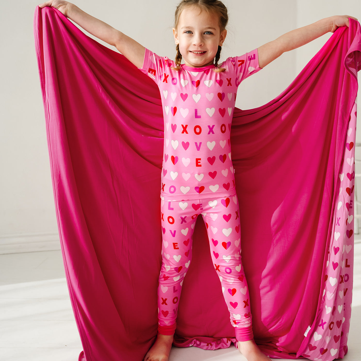 child posing wearing a Pink XOXO two piece pajama set holding up a matching large cloud blanket showing off the solid pink backing
