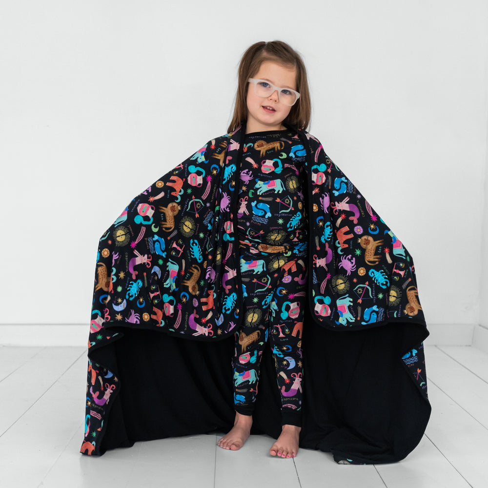 Image of a child holding a Star Signs blanket and wearing a matching printed two piece pj set