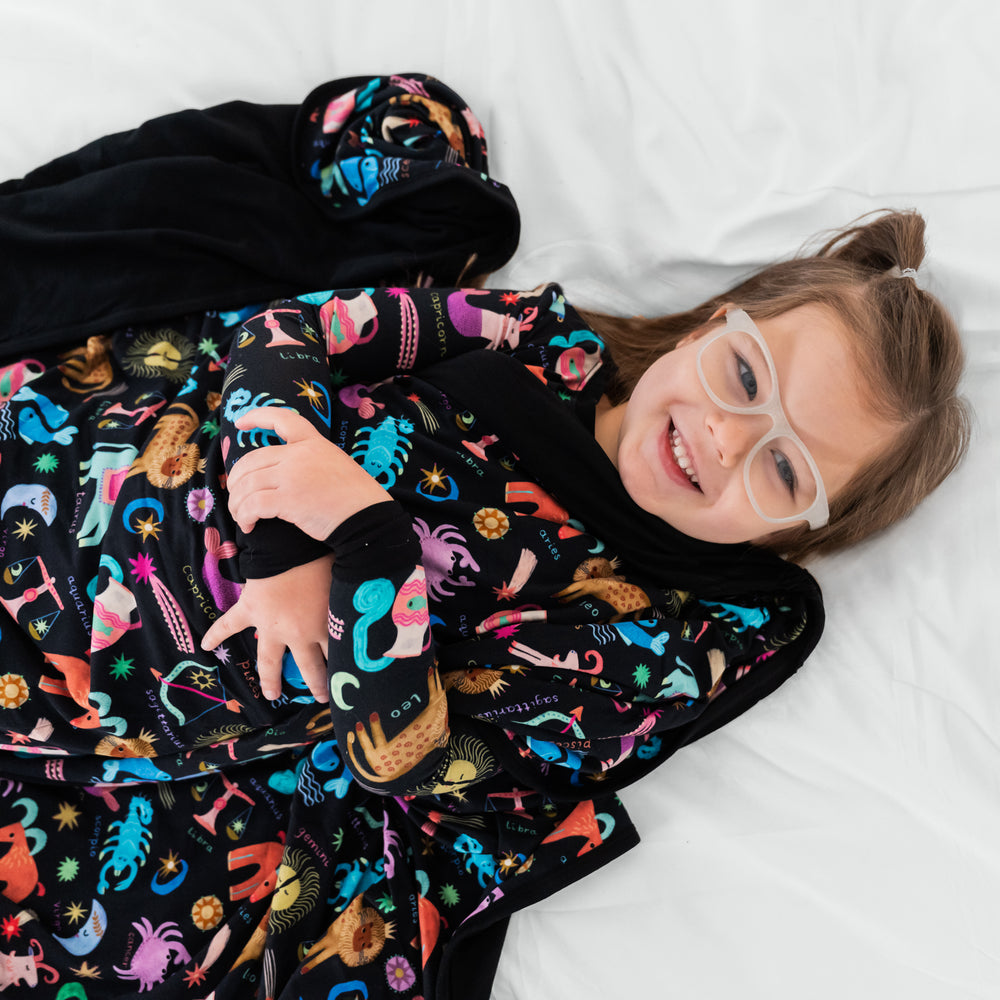 Image of a child snuggled up with the Star Signs blanket wearing a matching two piece pj set.