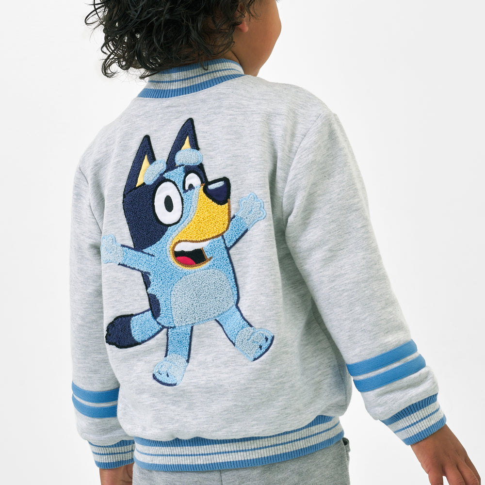 Close up back view image of a child wearing a Bluey gray bomber jacket