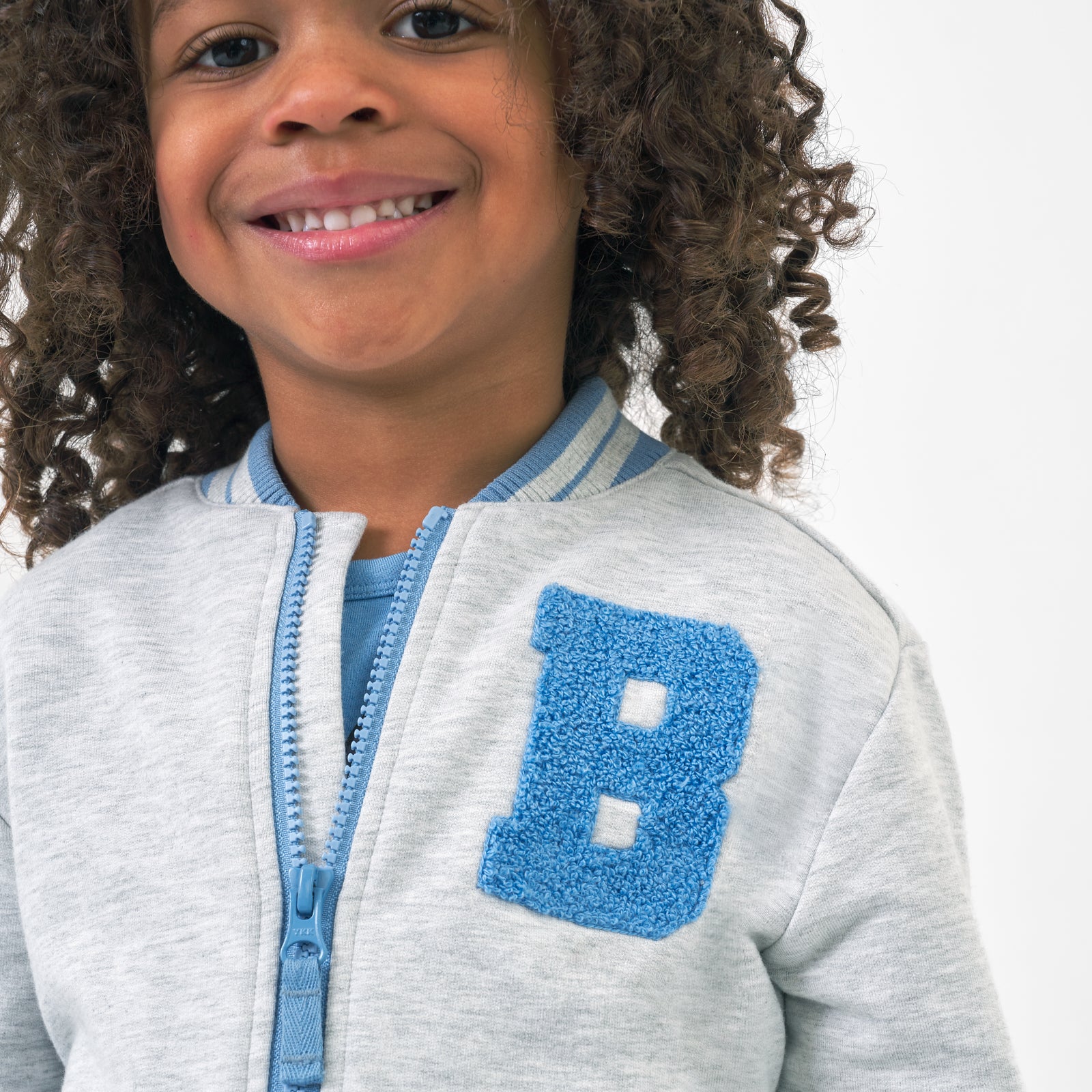 Close up image of a child wearing a Bluey gray bomber jacket detailing the B lettering