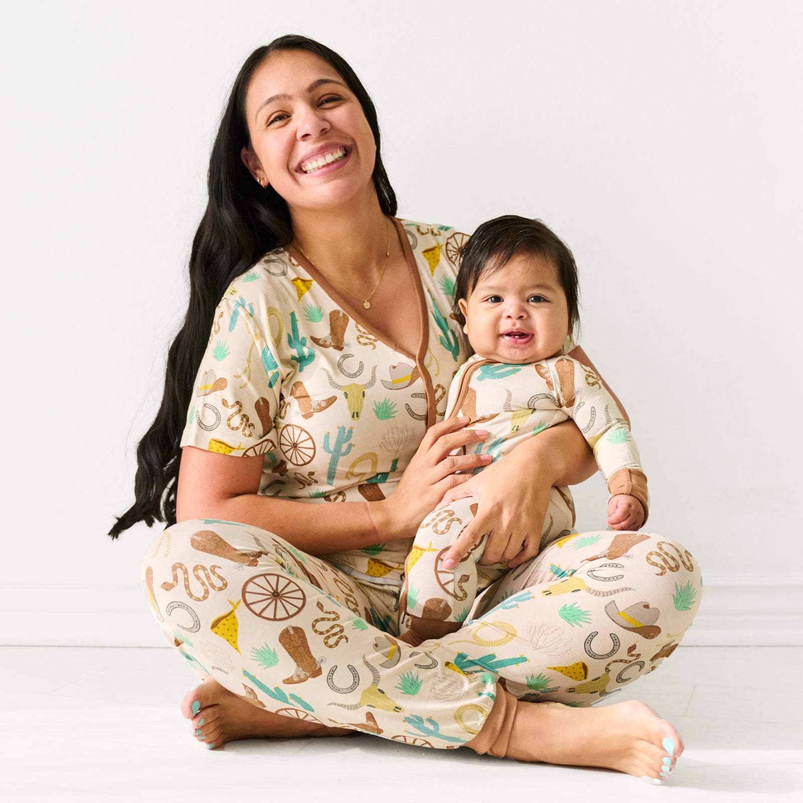 Mother sitting and holding her child. Mom is wearing women's Caramel Ready to Rodeo women's pj top and matching pj pants. Her daughter is wearing a matching zippy