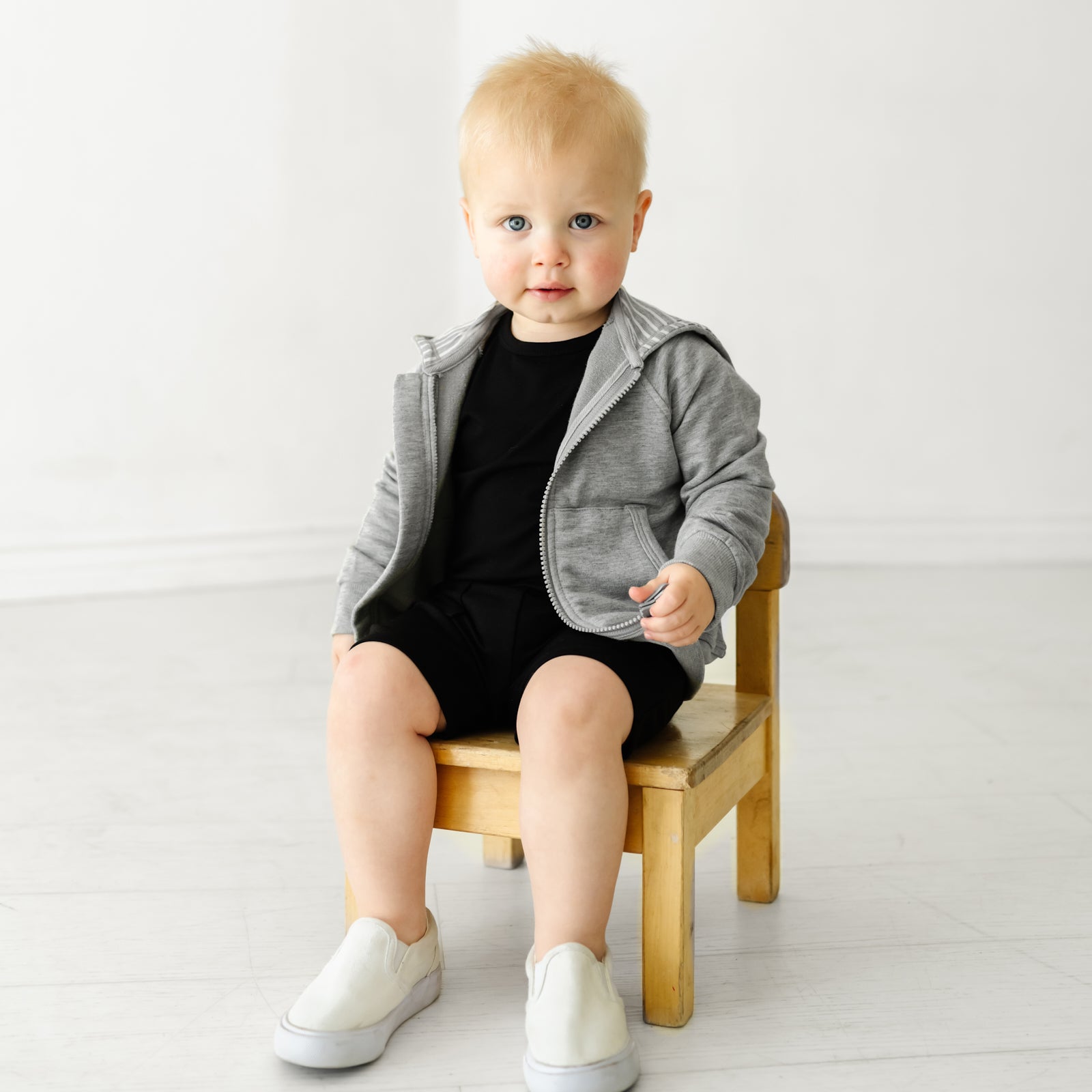 Child sitting on a chair wearing Black shorts and coordinating Play top and zip hoodie