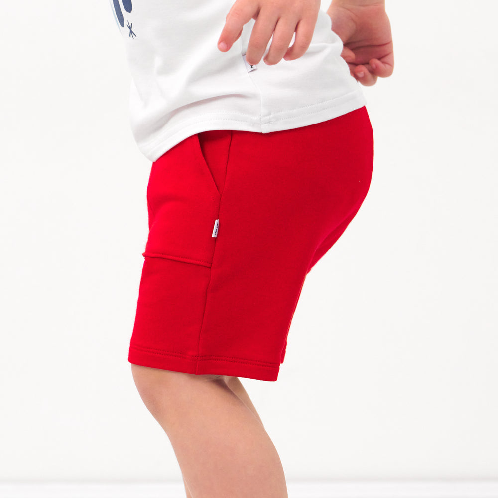 Close up side view image of a child wearing Candy Red shorts and coordinating Play tops