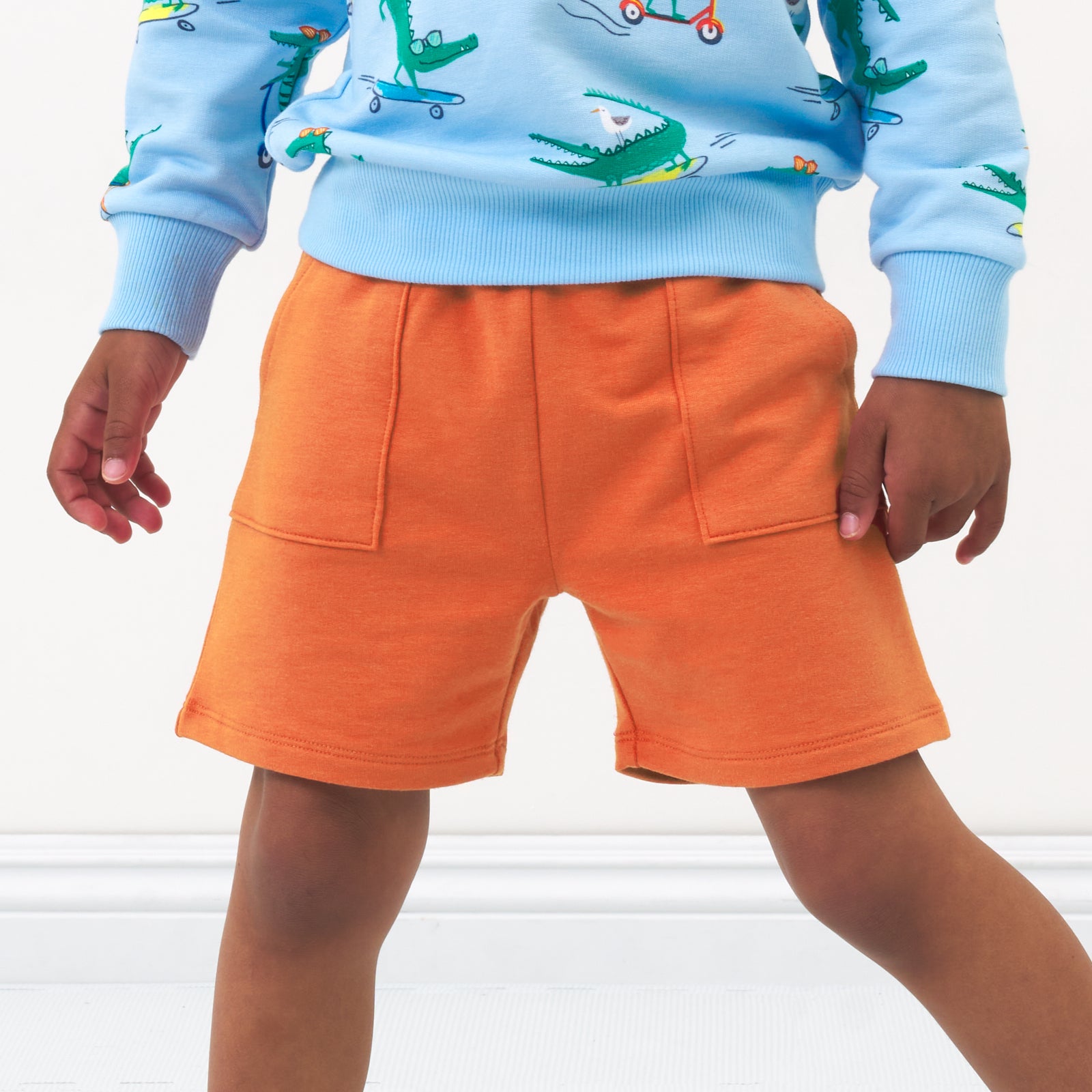 Close up image of a child wearing Rust Orange shorts and a coordinating crewneck sweatshirt