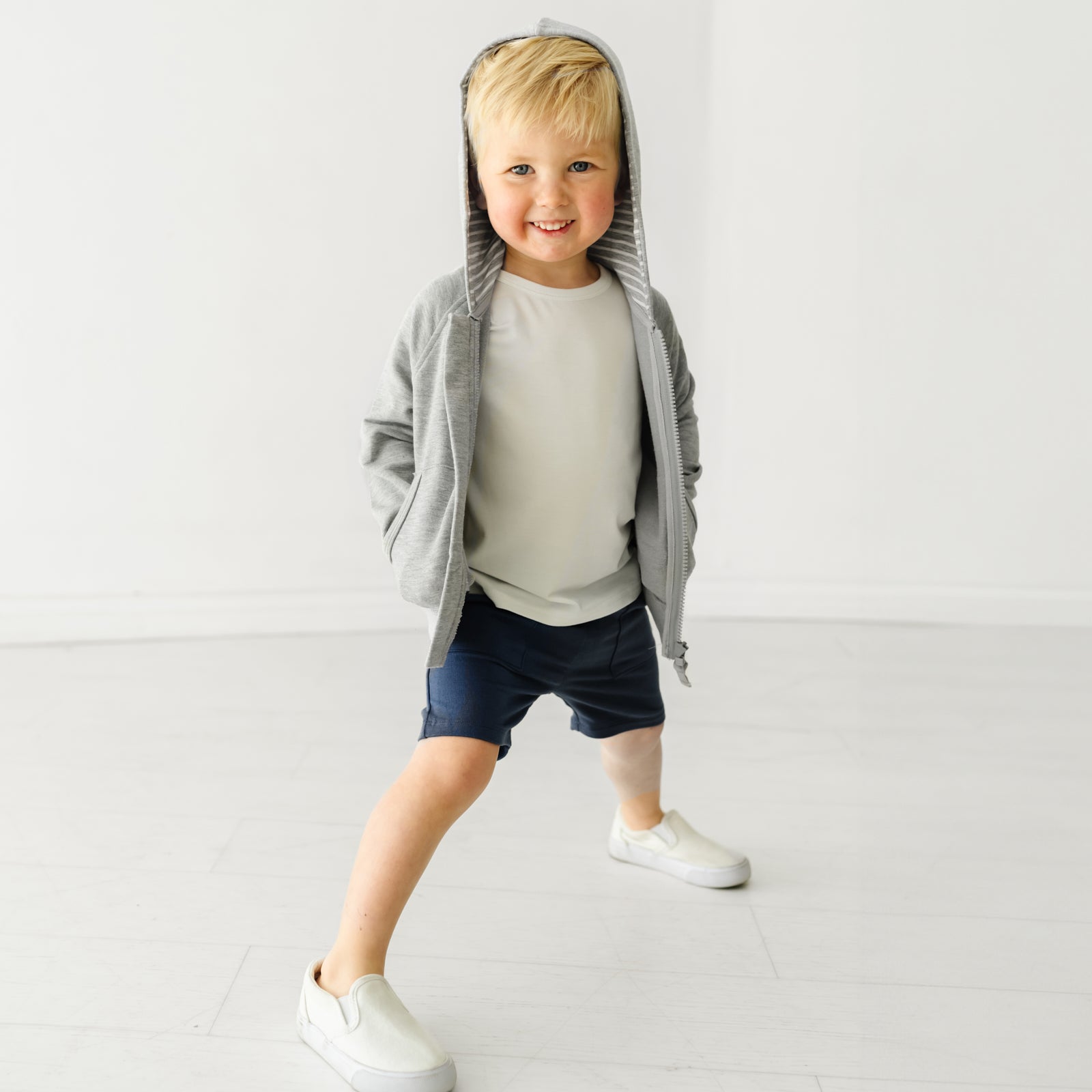 Child wearing Vintage Navy shorts and coordinating Play top and zip up hoodie with the hood up