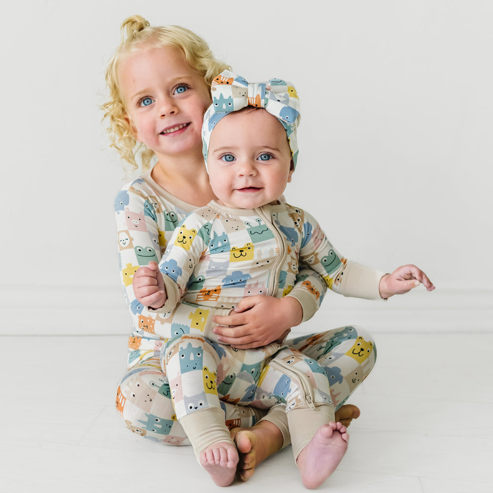 Two children sitting together wearing matching Check Mates pjs and a matching luxe bow headband