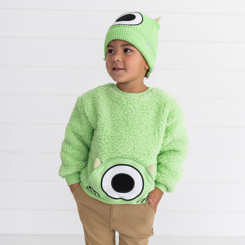 Child posing while wearing the Disney Monsters, Inc. Mike Wazowski Sherpa Pocket Crewneck and Disney Monsters, Inc. Mike Wazowski Beanie Hat