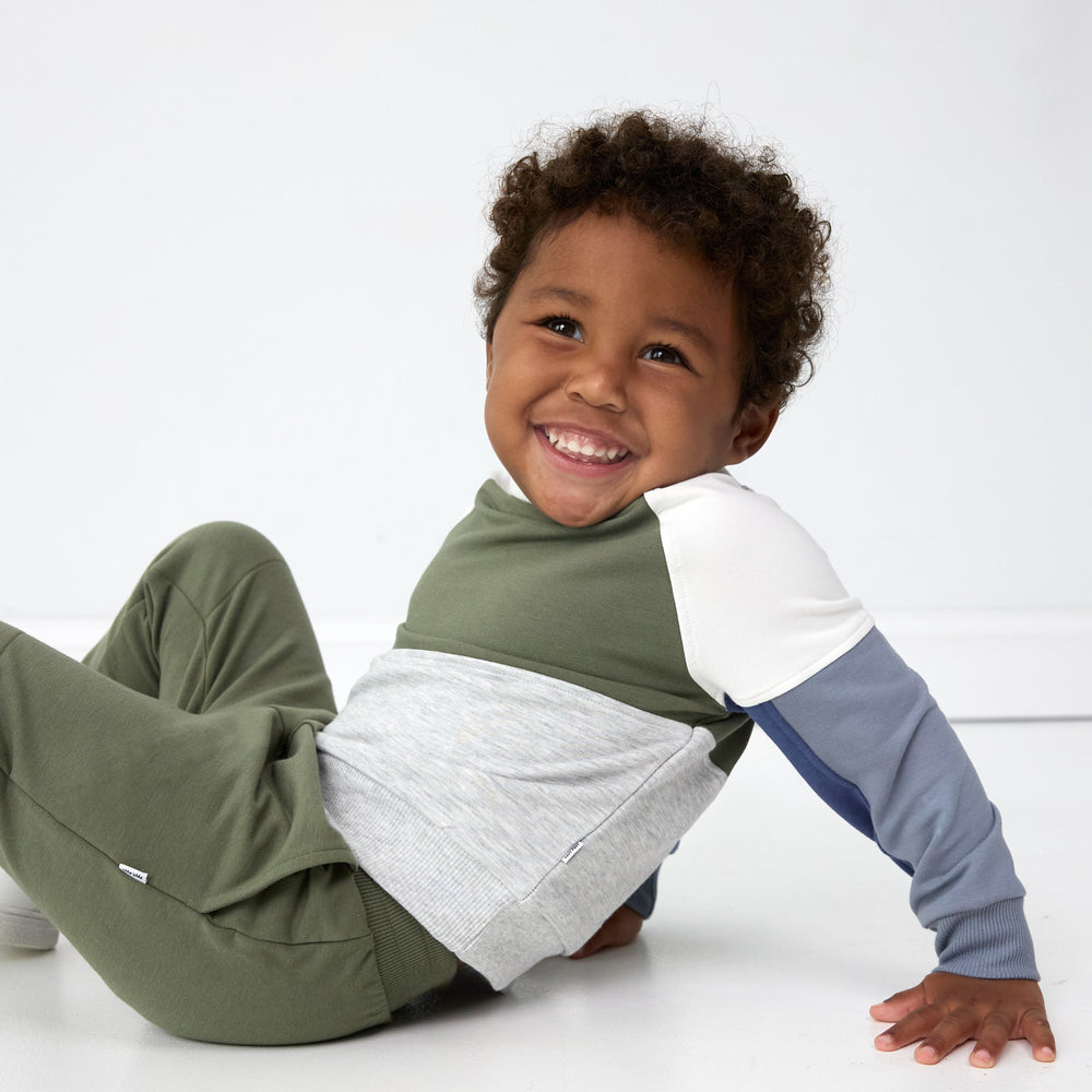 Smiling boy sitting down and wearing the Olive Panel Crewneck and Olive Jogger