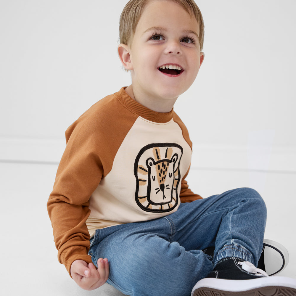 Child sitting on the ground wearing an Arctic raglan crewneck paired with denim joggers