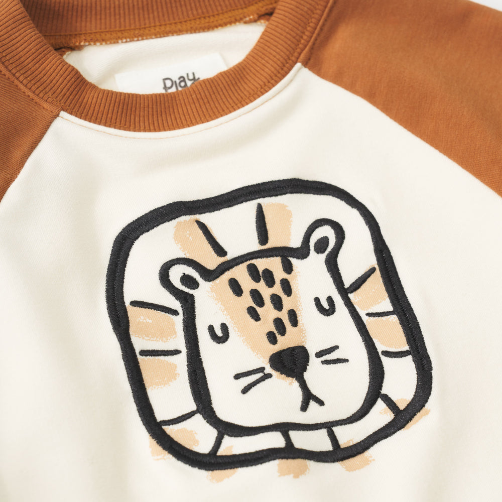 Close up view of the black and tan lion illustration on an Arctic raglan crewneck