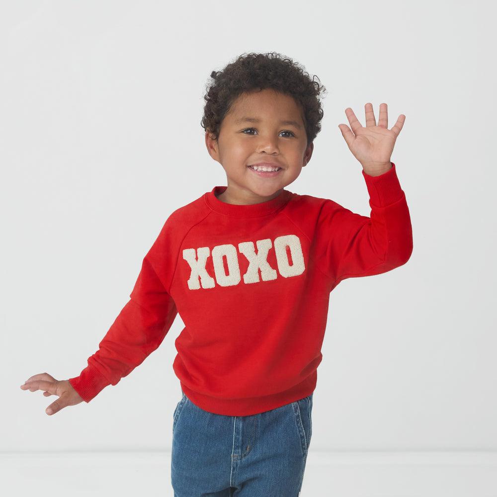 Waving child wearing an XOXO Crewneck Sweatshirt and coordinating denim jogger