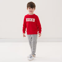 Child wearing a Candy Red crewneck sweatshirt and coordinating Heather Gray jogger