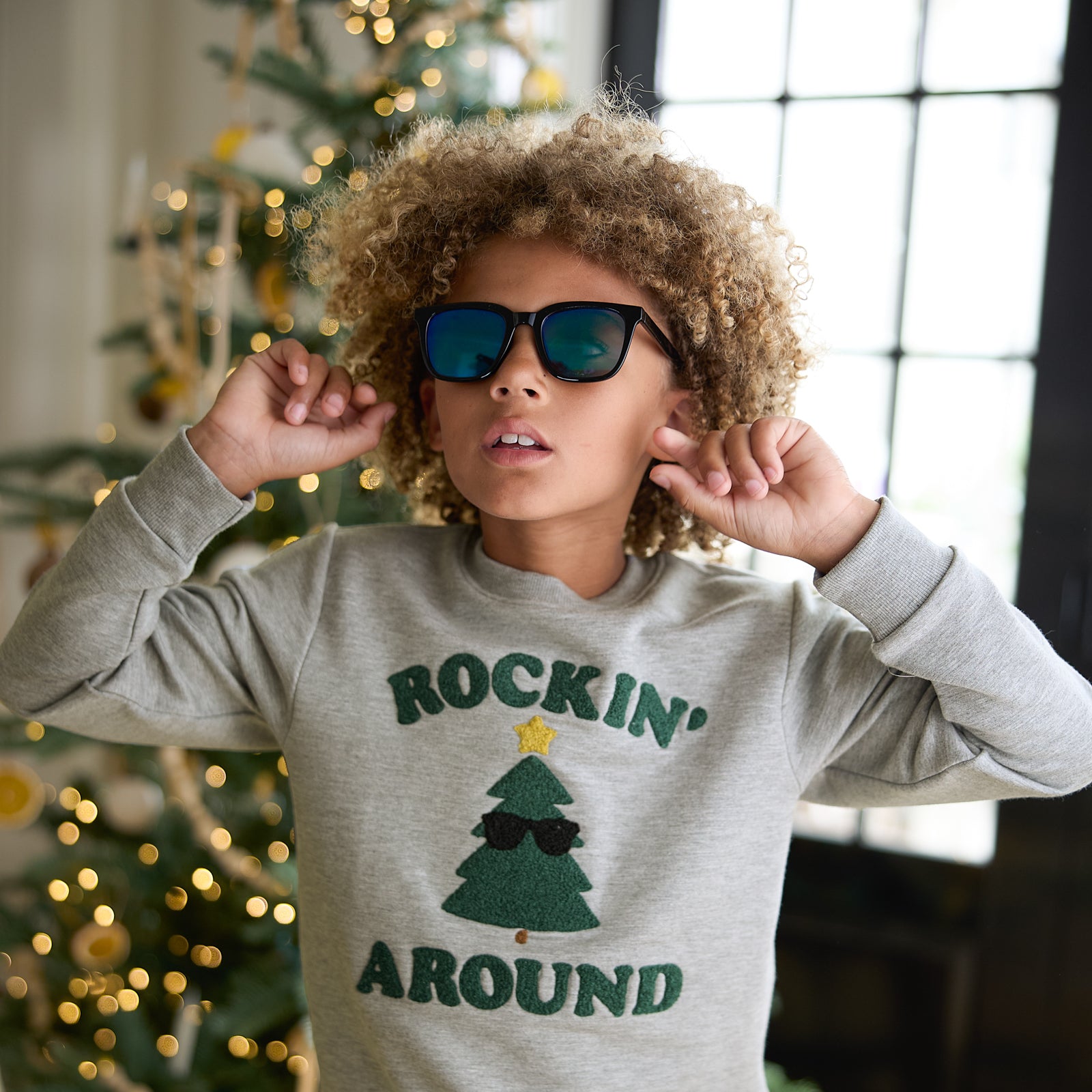 Close up image of a child wearing a Rockin' Around Crewneck Sweatshirt and sunglasses