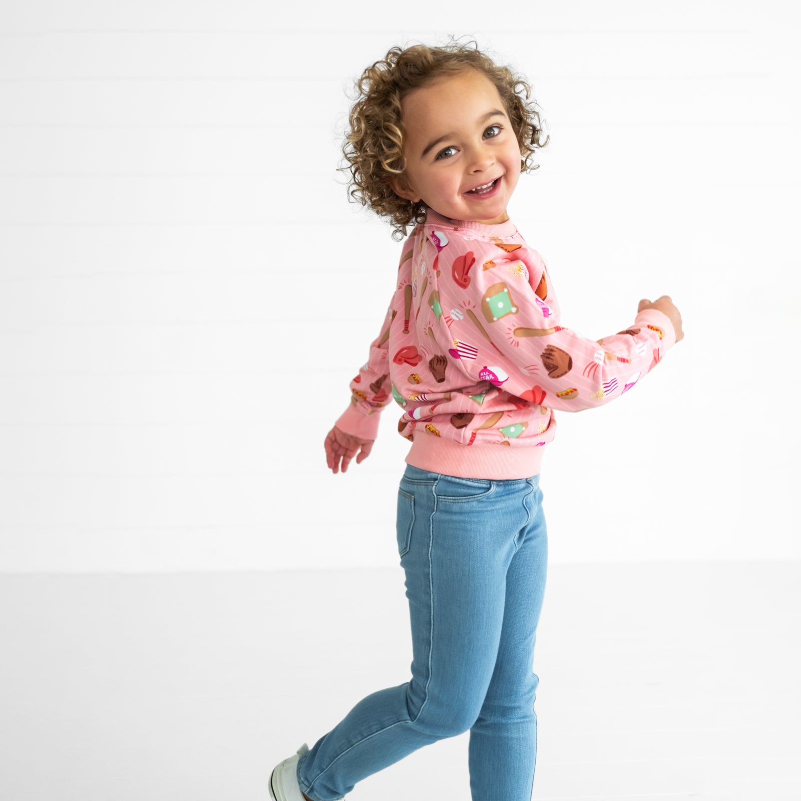 Side view image of a child wearing a Pink All Stars Crewneck Sweatshirt and Light Blue Denim Jegging