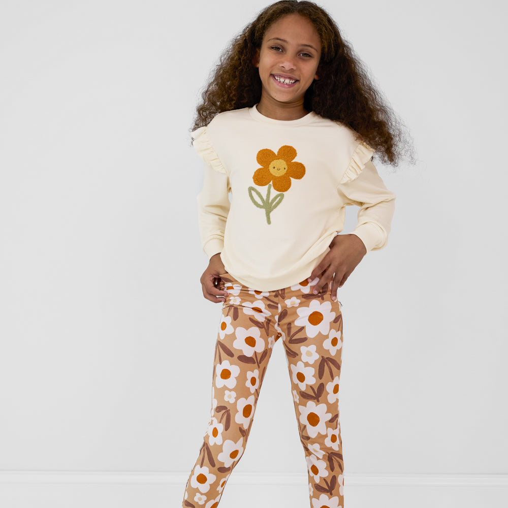 Child with her hands on her hips wearing an Arctic Flutter Crewneck featuring a daisy, paired with tan floral leggings