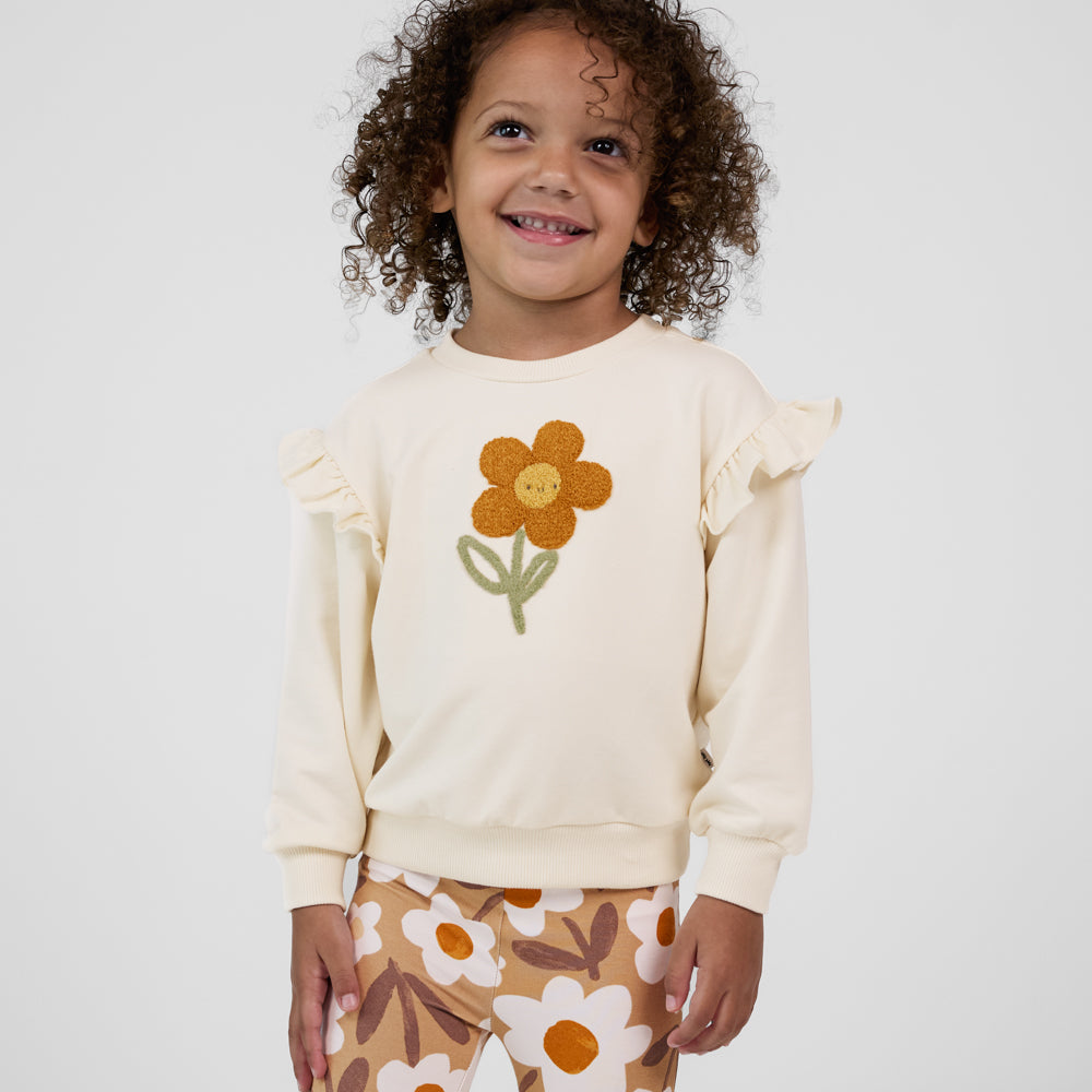 Child looking up and smiling wearing an Arctic Flutter Crewneck featuring a daisy, paired with tan floral leggings