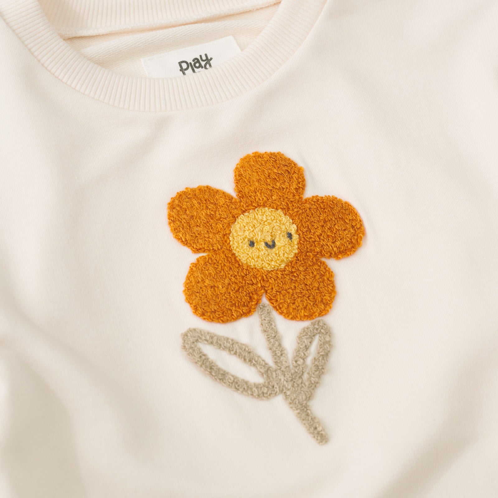 Close-up view of the orange and yellow daisy on an Arctic Flutter Crewneck