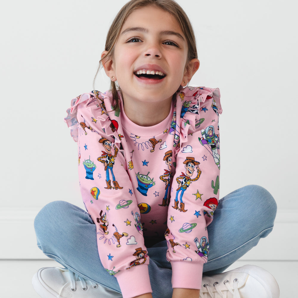 Child sitting on the ground wearing a Disney & Pixar Toy Story Stars Flutter Crewneck and Light Blue Denim Jegging