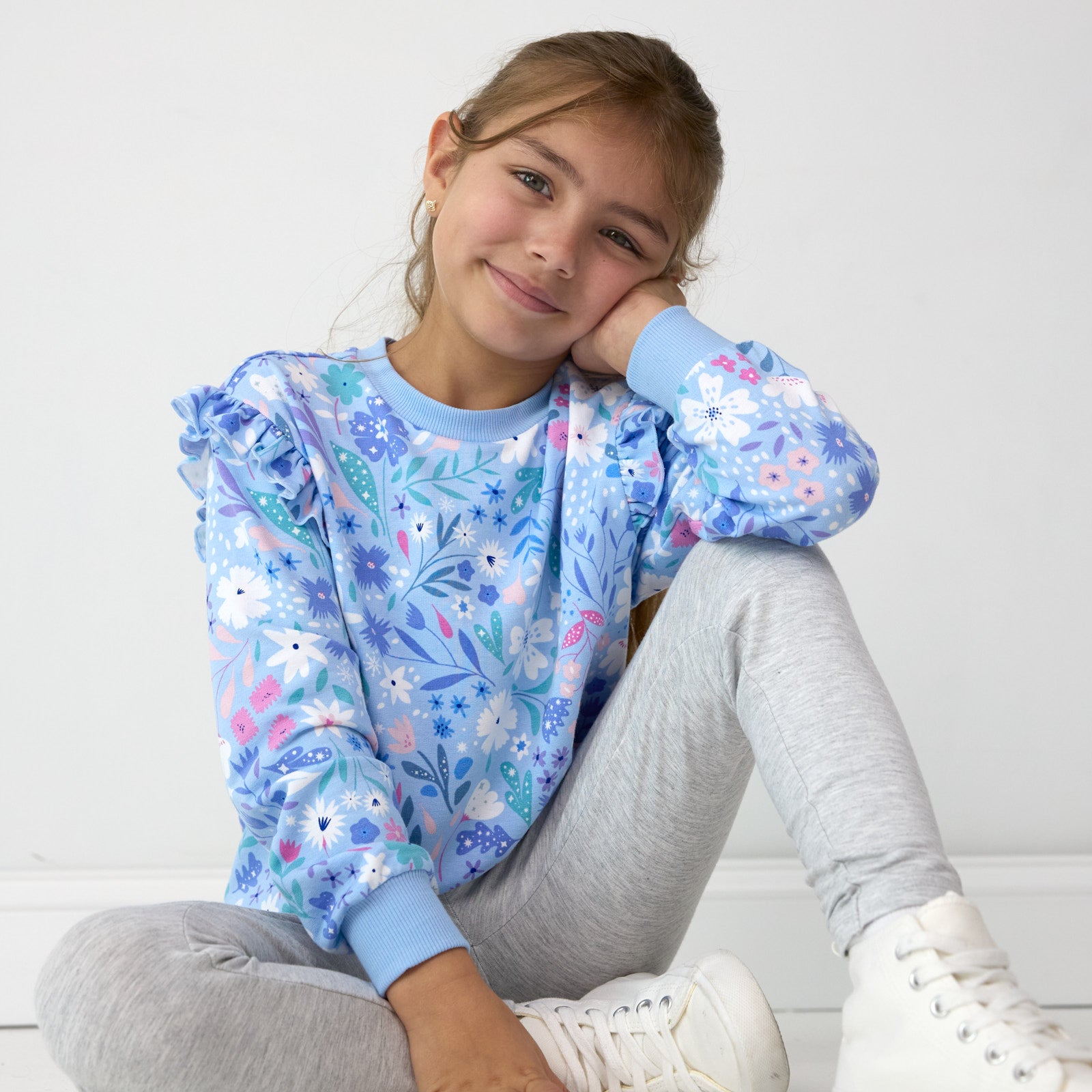 Smiling girl posing while sitting down and wearing the Magical Meadow Flutter Crewneck and Light Heather Gray Legging