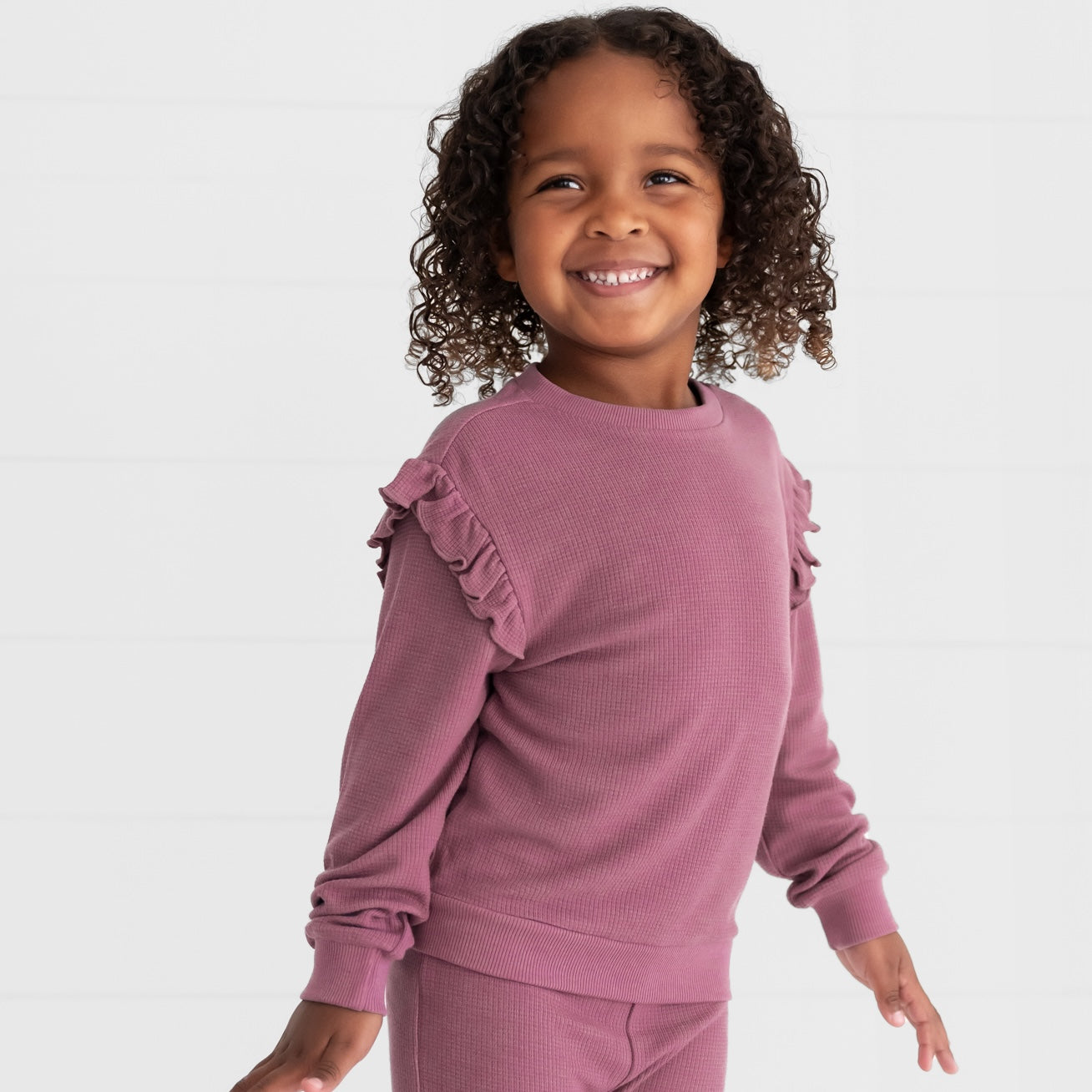 Close up image of a child wearing a Dusty Plum Waffle Flutter Crewneck and matching Waffle Flare Pants