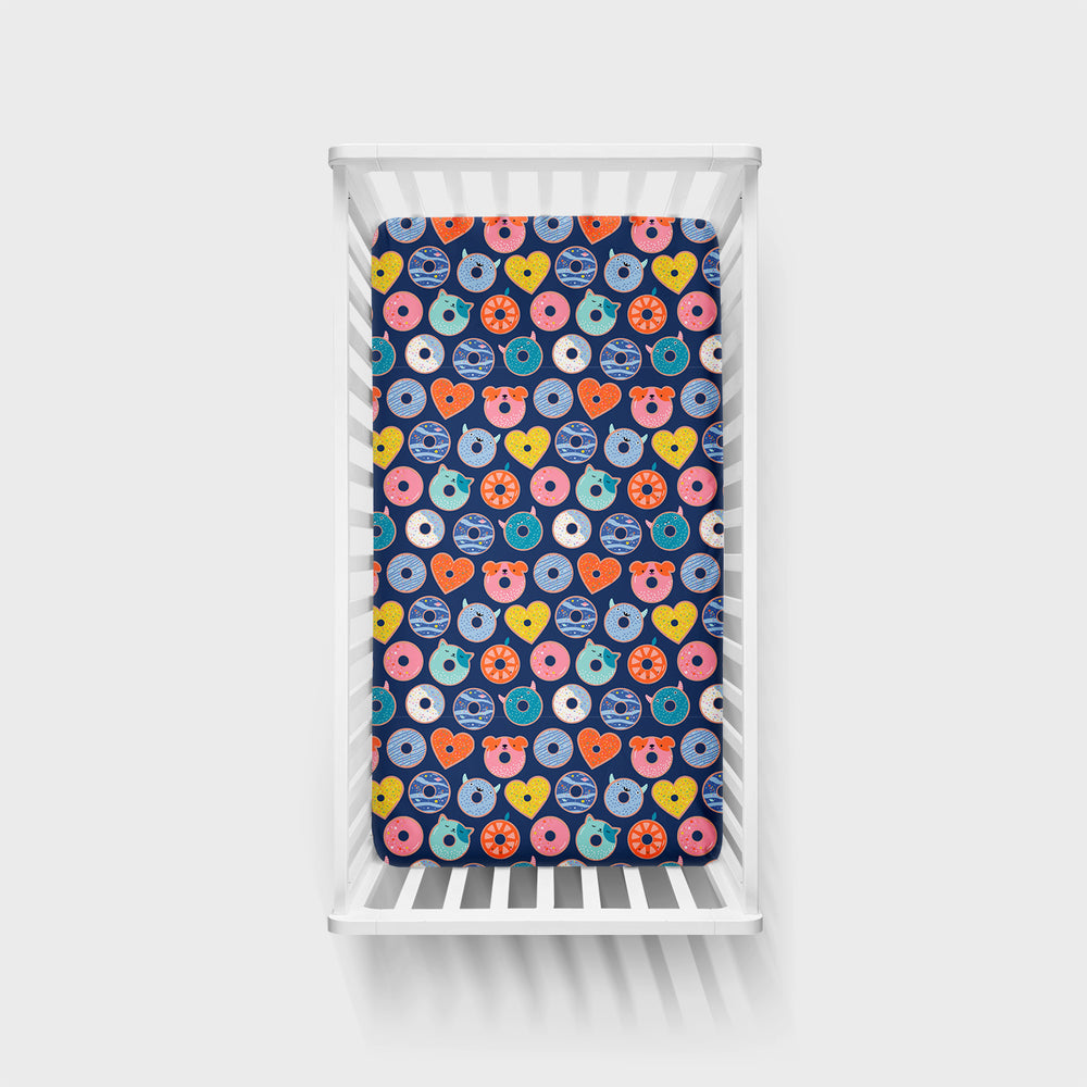 Click to see full screen - Top view of a Blue Donut Dreams fitted crib sheet in a white crib