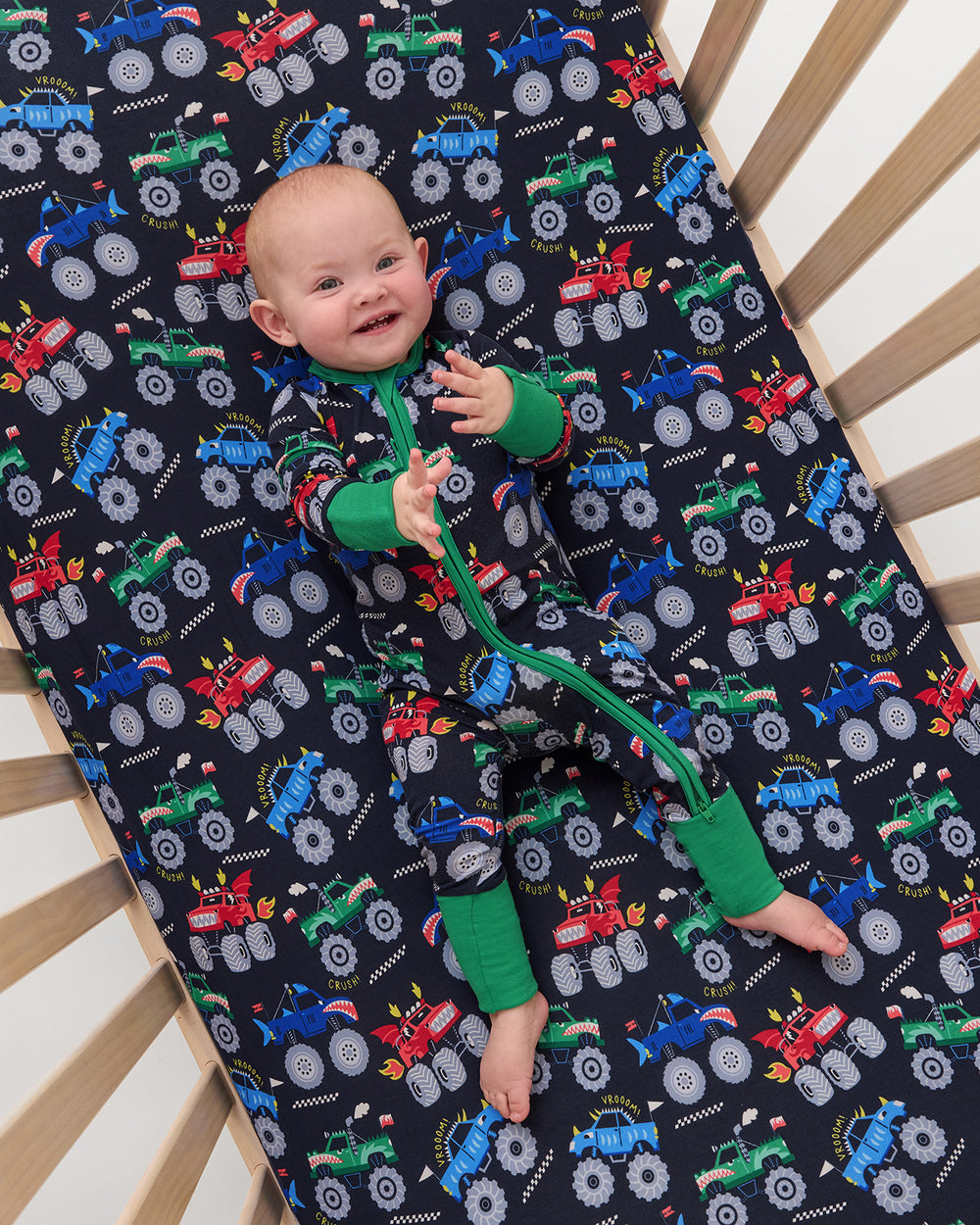Aerial view of baby laying on the Monster Truck Madness Fitted Crib Sheet