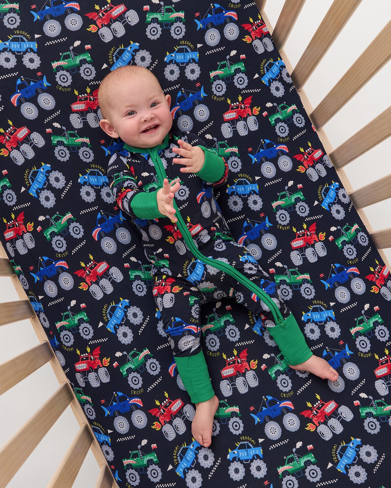 Aerial view of baby laying on the Monster Truck Madness Fitted Crib Sheet