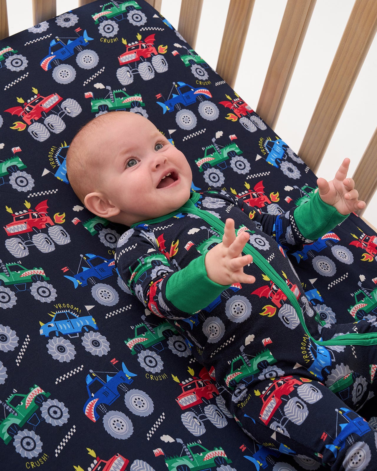 Close up of baby laying on the Monster Truck Madness Fitted Crib Sheet in a matching footie pajama
