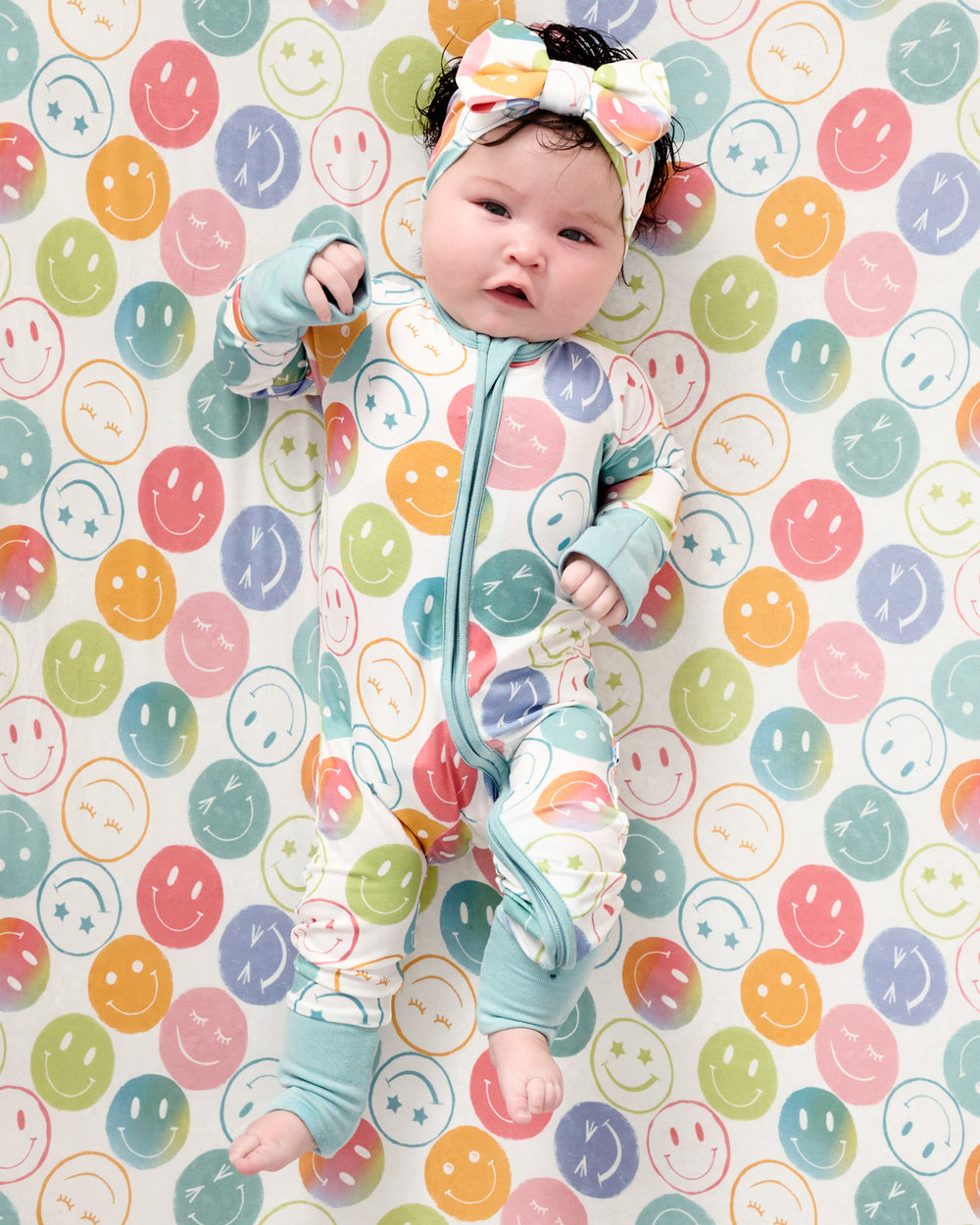 Aerial view of baby wearing the Positive Vibes Zippy and Luxe Bow Headband on a matching crib sheet