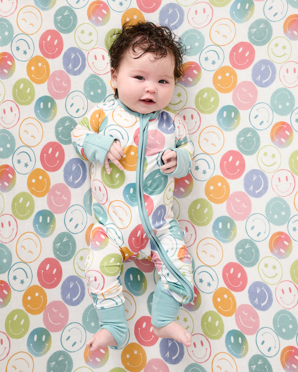 Baby wearing the Positive Vibes Zippy on a matching crib sheet