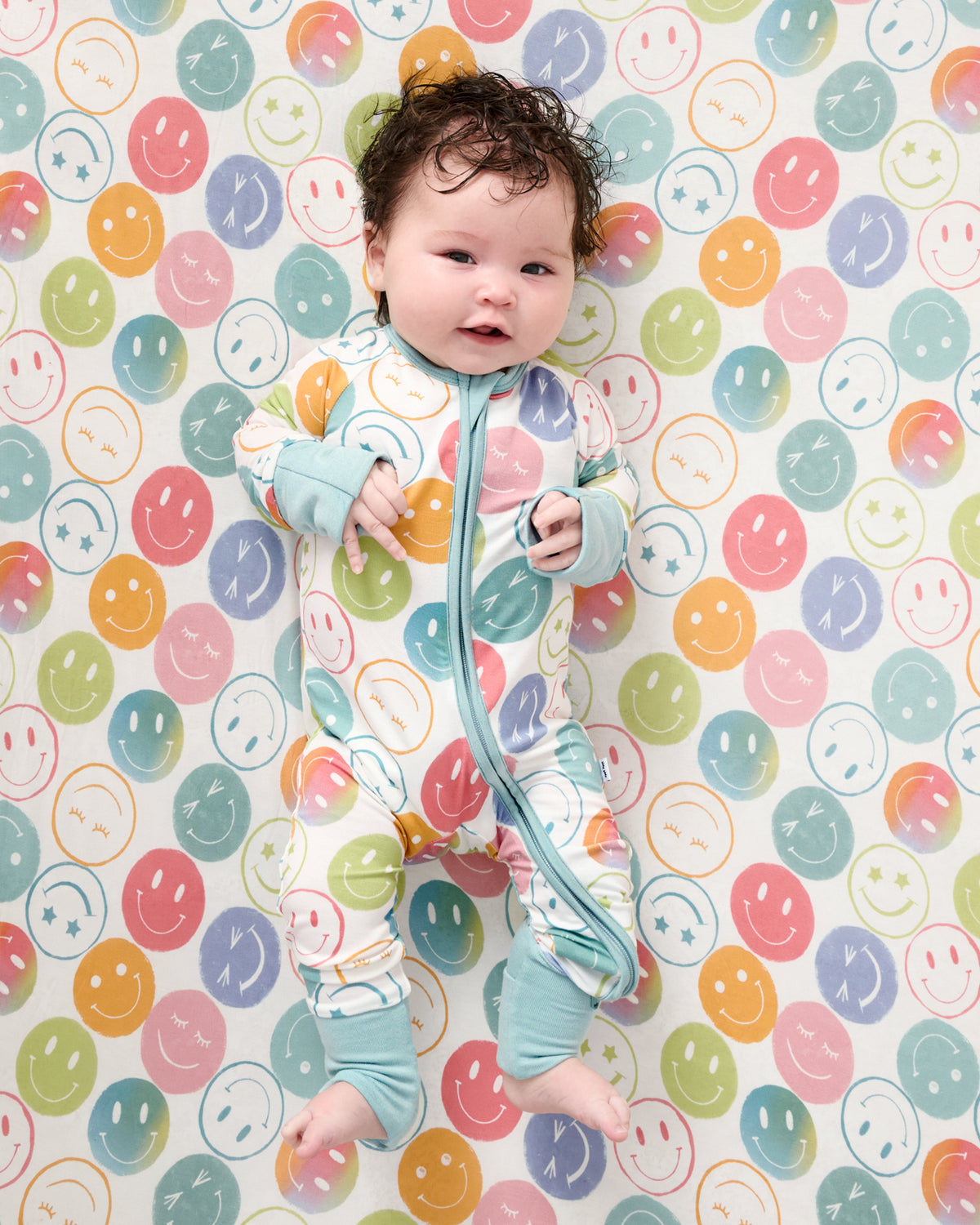 Baby wearing the Positive Vibes Zippy on a matching crib sheet