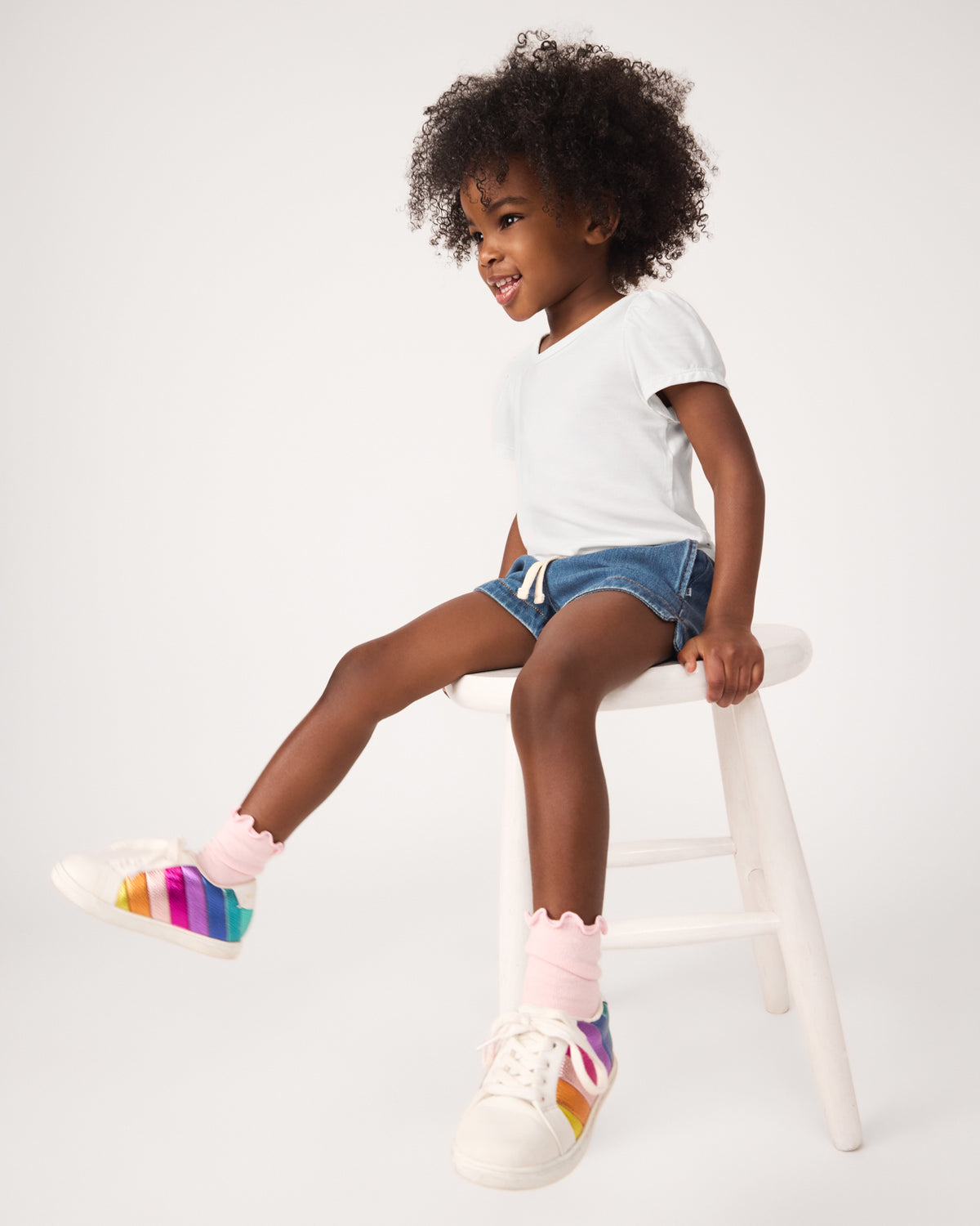 Girl sitting on a stool wearing the Soft White Puff Sleeve Tee with denim drawstring shorts