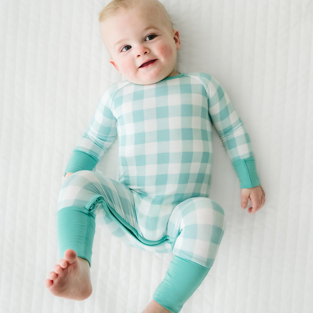 Click to see full screen - Child laying on a bed wearing a Aqua Gingham crescent zippy