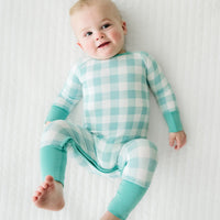Child laying on a bed wearing a Aqua Gingham crescent zippy