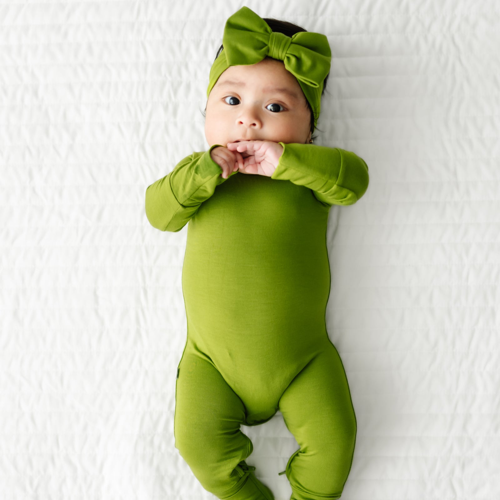 Child laying on a bed wearing an Avocado Crescent zippy paired with a luxe bow headband