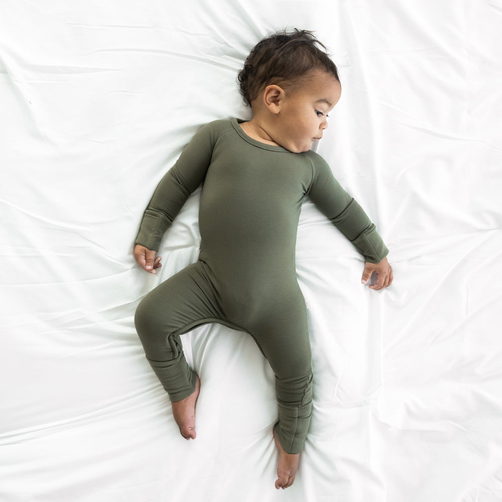 Child laying on a bed wearing a Cozy Olive crescent zippy