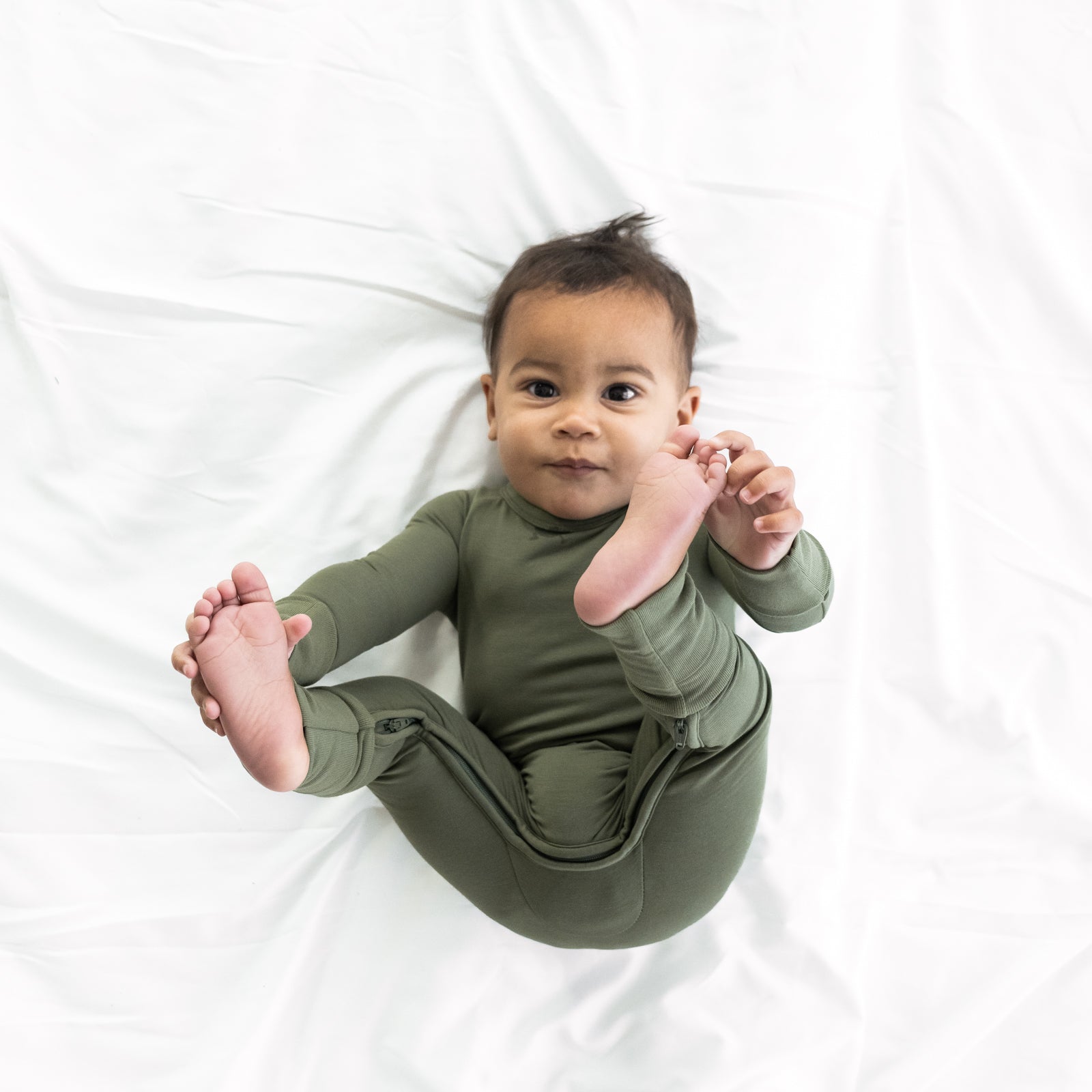 Alternate image of a child laying on a bed wearing a Cozy Olive crescent zippy