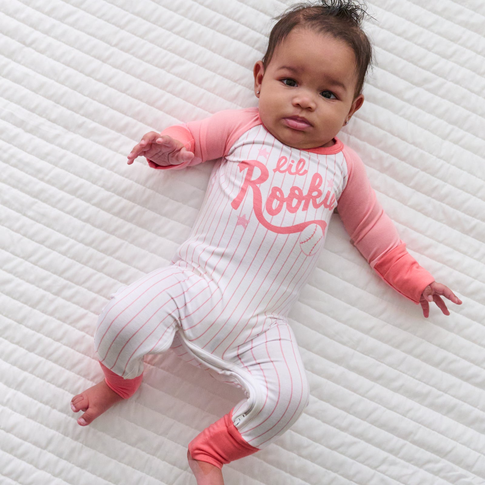 Child laying on a bed wearing a pink Little Rookie crescent zippy