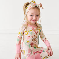 Child sitting wearing a Pink Ready to Rodeo Crescent Zippy paired with a matching luxe bow headband