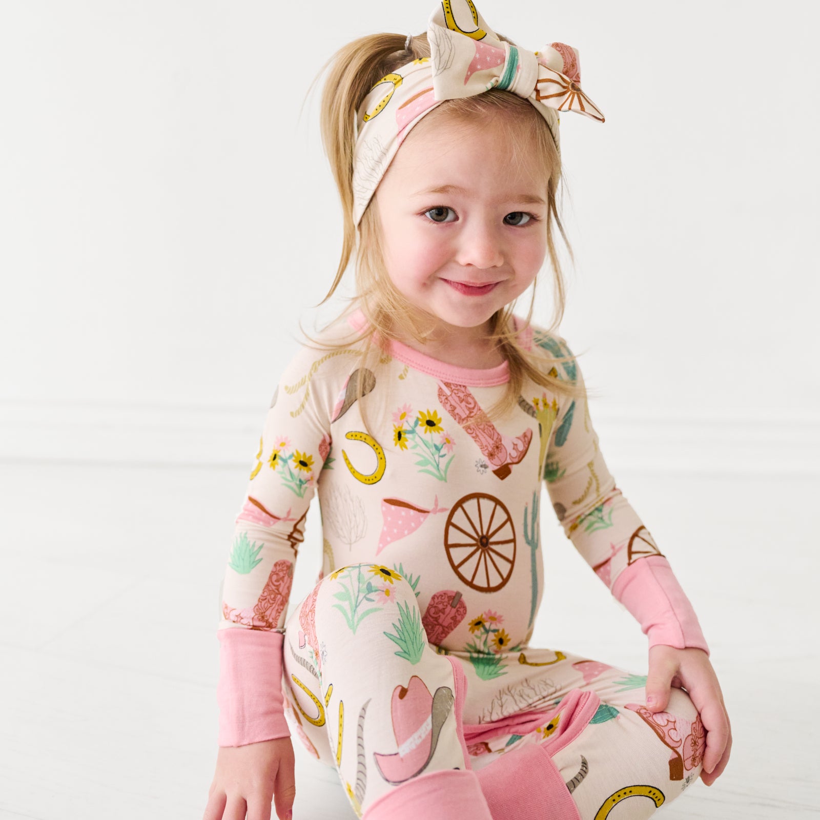 Child wearing a Pink Ready to Rodeo crescent zippy paired with a matching luxe bow headband