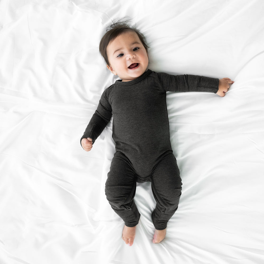 Child laying on a bed wearing a Cozy Heather Black crescent zippy