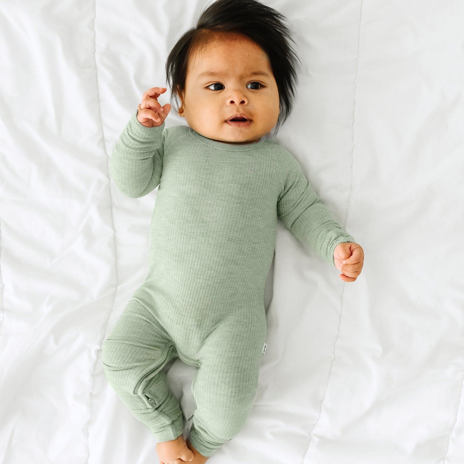 Child laying on a bed wearing a Heather Sage crescent zippy